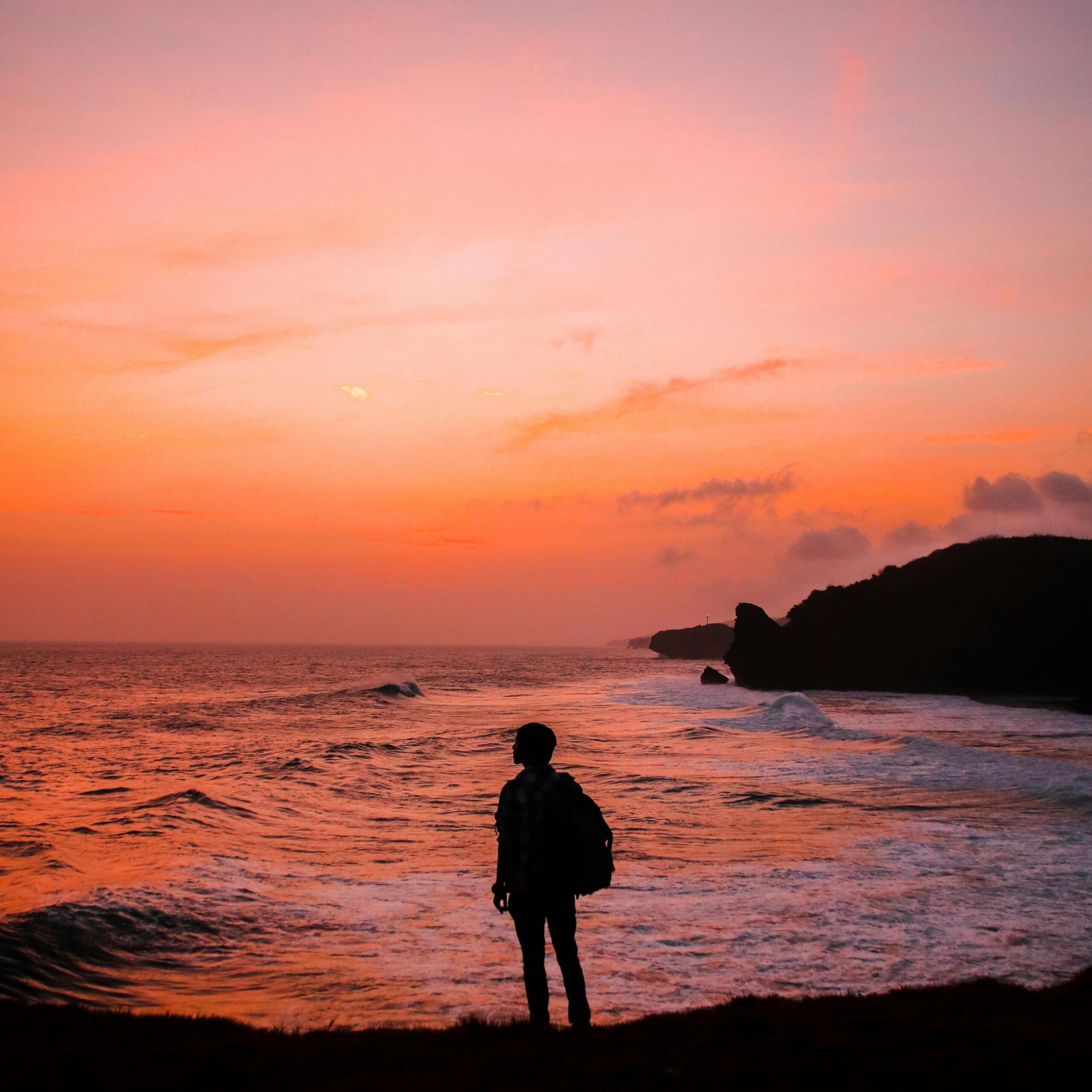 Silhouette of a person with a backpack against a vibrant Indonesian sunset by the sea.